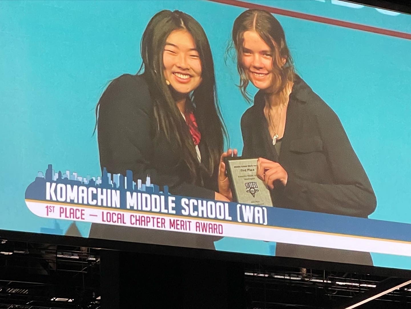 FBLA National Secretary, Grace Zhang (left) with KMS Chapter Secretary Alyssa Childers are shown on the projection screen at the McCormick Place Convention Center in Chicago at the FBLA conference receiving the Award for the school chapter.